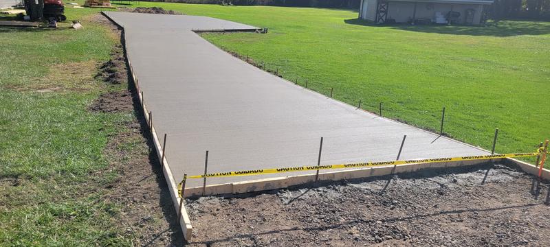 Freshly poured broom-finish concrete driveway ribbon across a yard